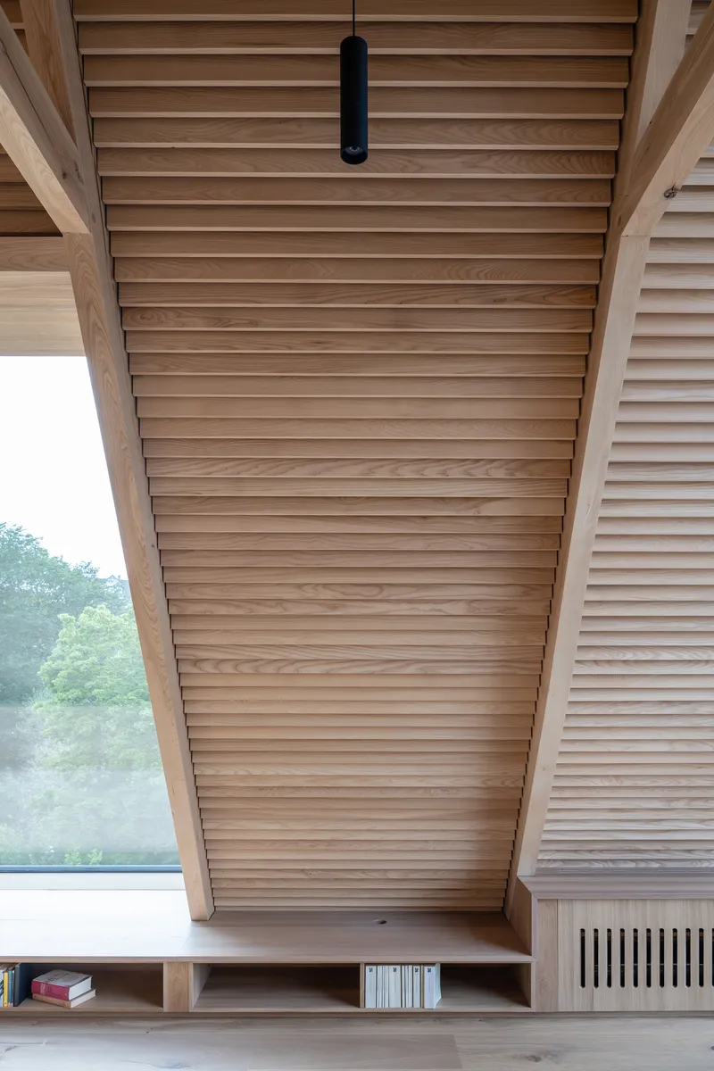 Sloped timber-slatted ceiling over built-in bench with window opening to greenery outside