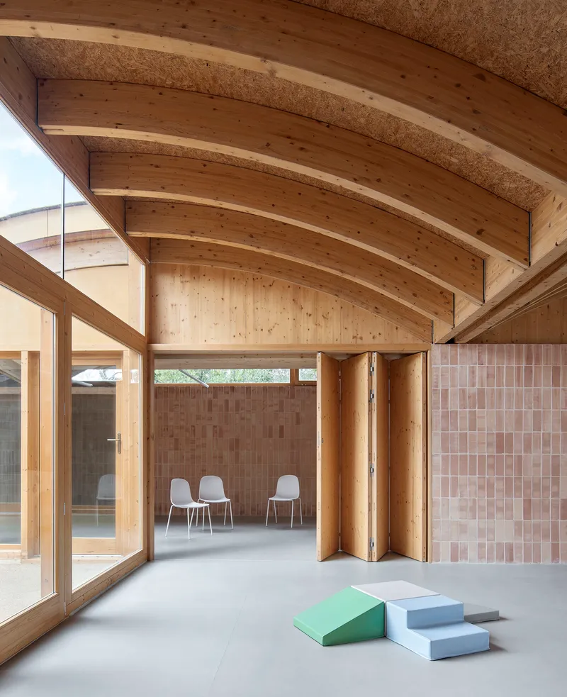 Corner view showing curved timber rafters, folding timber screens, and foam play blocks on the floor