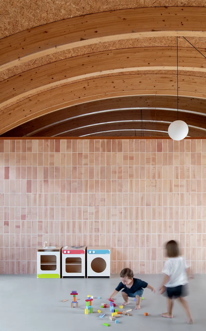 Pink tiled wall with children playing on the polished concrete floor beneath arched timber beams