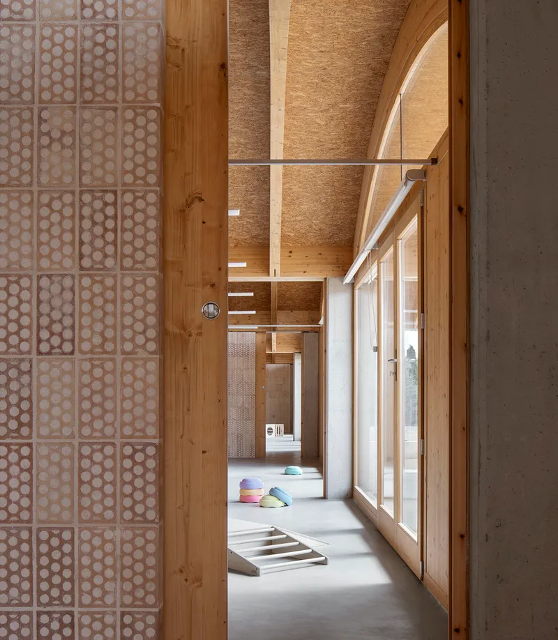 Interior corridor with exposed timber ceiling beams and patterned screen partition alongside a concrete wall