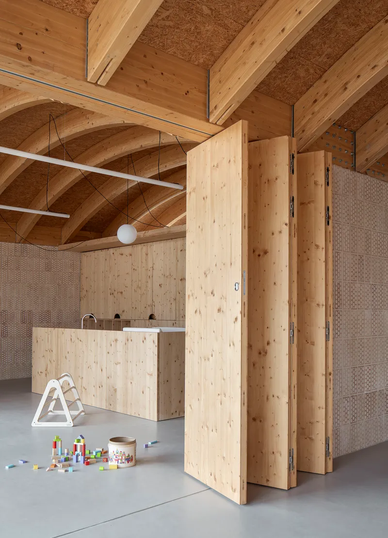 Interior space showing folding timber partitions beneath vaulted wooden ceiling with scattered toys on the floor