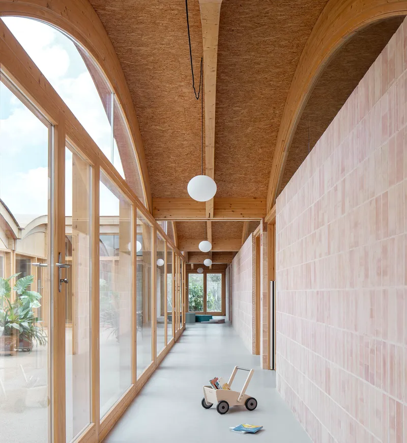 Corridor with arched timber roof and tiled wall alongside glazed courtyard with sphere pendant lights