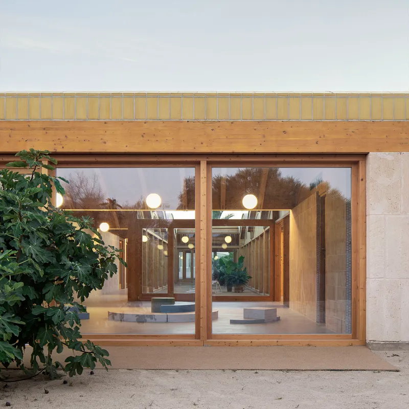 Glazed facade with timber frames revealing illuminated interior and suspended globe lights at dusk