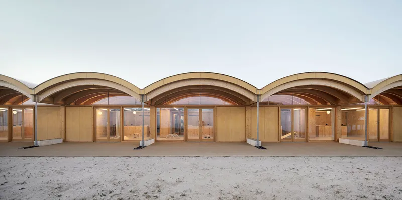 Covered colonnade with repeated arched timber vaults and glazed timber doors opening onto a sandy courtyard