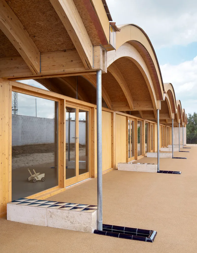 Angled view of the covered walkway showing timber columns and arched vaults under a partly cloudy sky