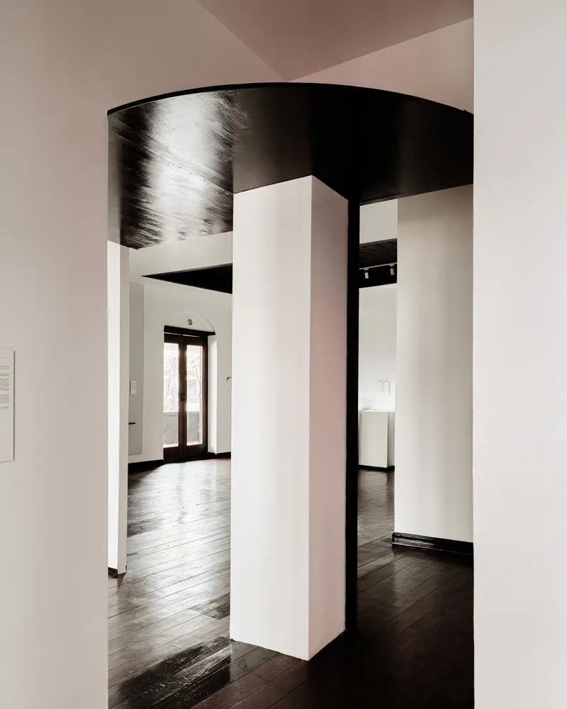 White partition walls beneath a curved black timber ceiling creating a sequence of doorways and passages