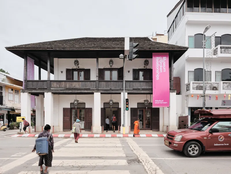 Two-storey colonial facade with timber balcony and pink exhibition banners on a street with pedestrians and traffic