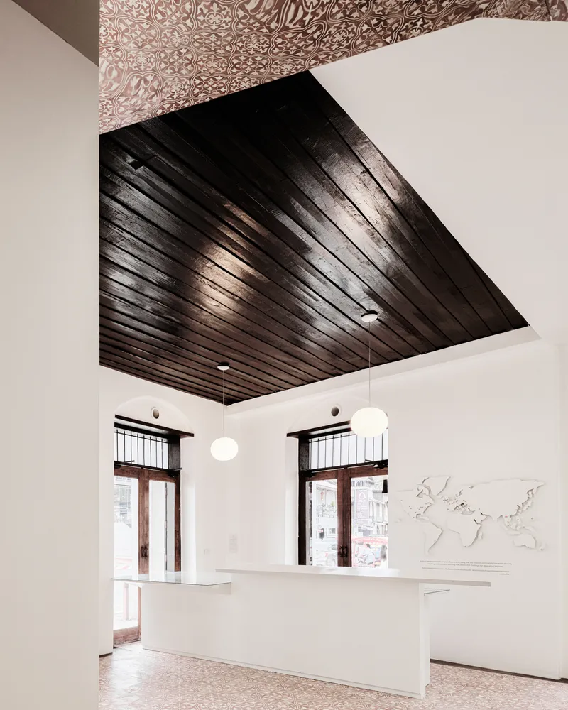 Reception desk under a dark timber slatted ceiling with patterned tile above and sphere pendant lights