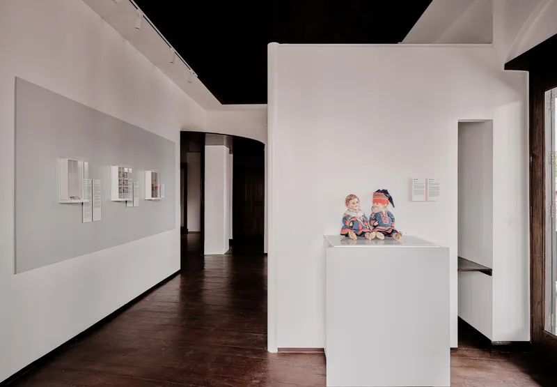 Gallery space with freestanding white partitions on dark timber floors with two children seated on a plinth