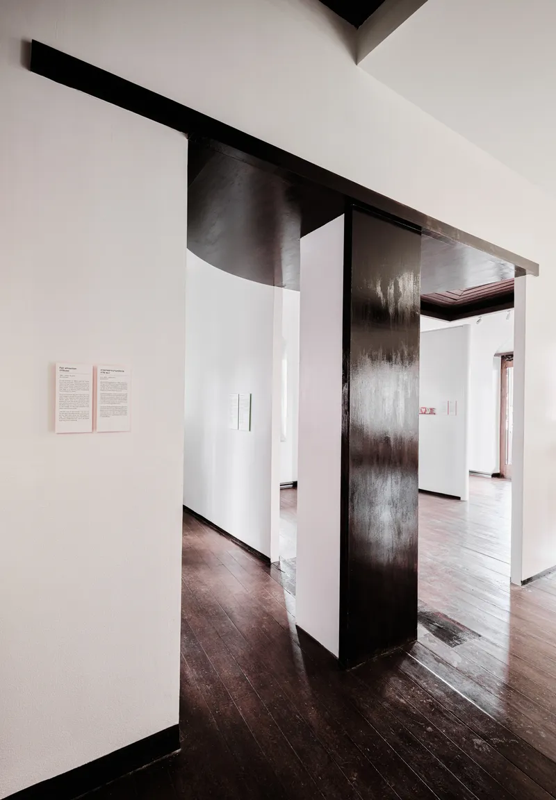 Blackened steel structural column framing a sequence of gallery doorways with dark timber floors