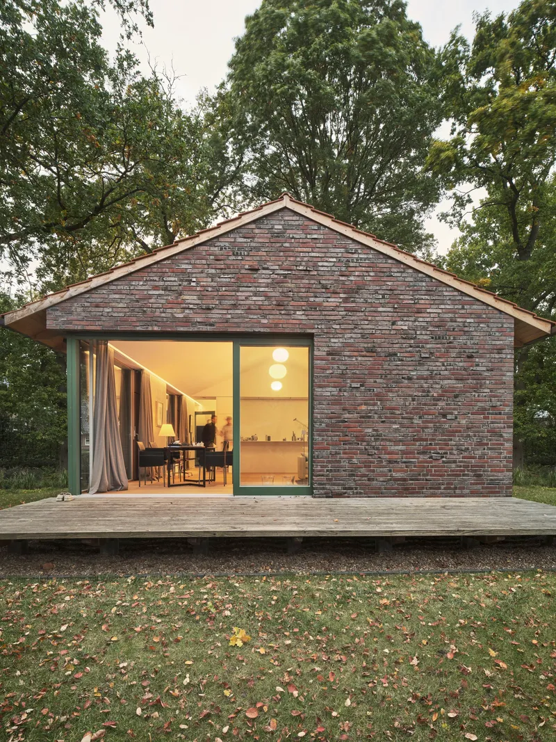 Reclaimed brick gable facade with full-height glazed opening onto timber deck surrounded by fallen autumn leaves