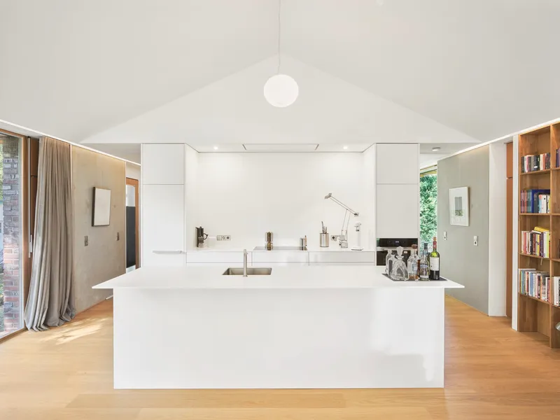 White kitchen island beneath vaulted ceiling with spherical pendant light and continuous perimeter slot lighting