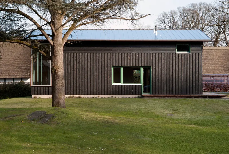 Corrugated timber facade with standing seam metal roof and mature deciduous tree in winter lawn