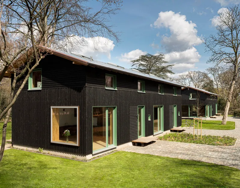 Black timber-clad facade with white window frames and lawn under a partly cloudy spring sky