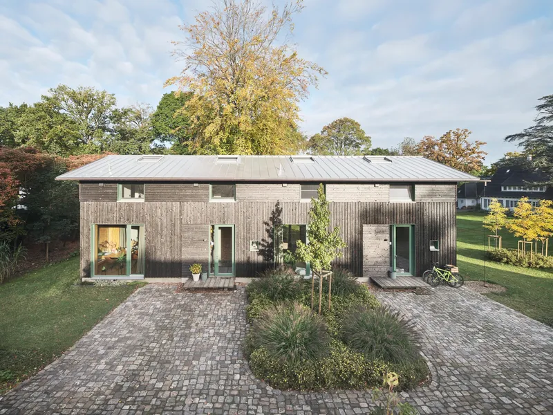 Entrance facade with corrugated timber cladding and planted cobblestone courtyard at dusk