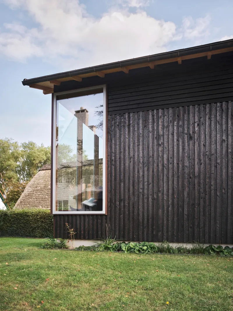 Detail of projecting window in charred timber cladding with eave overhang and lawn below