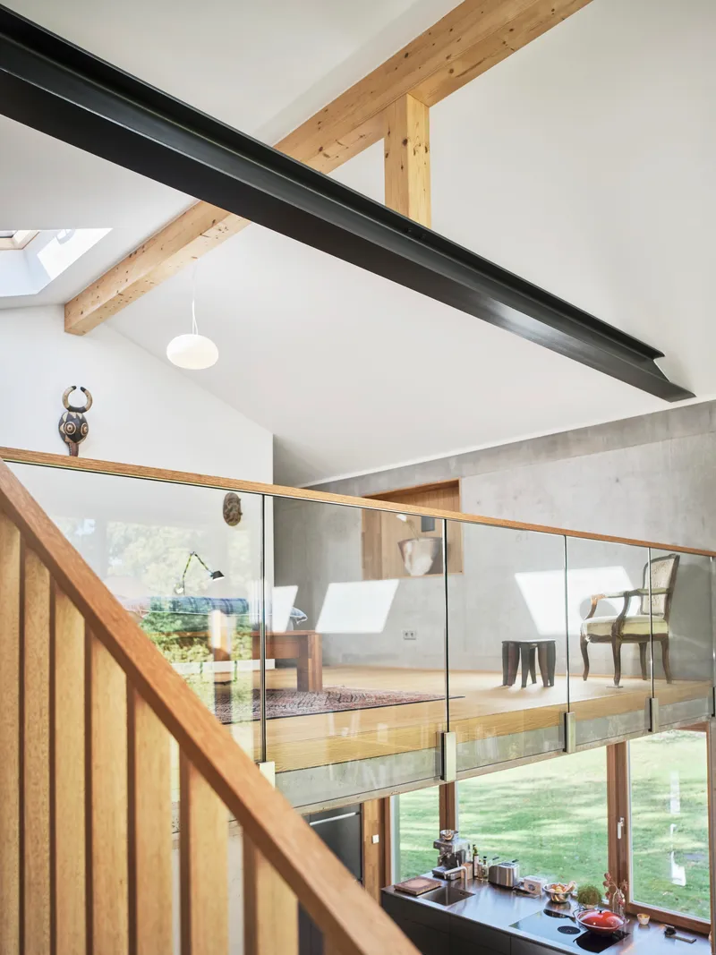 Upper level mezzanine with glass balustrade overlooking double-height space and exposed timber rafters