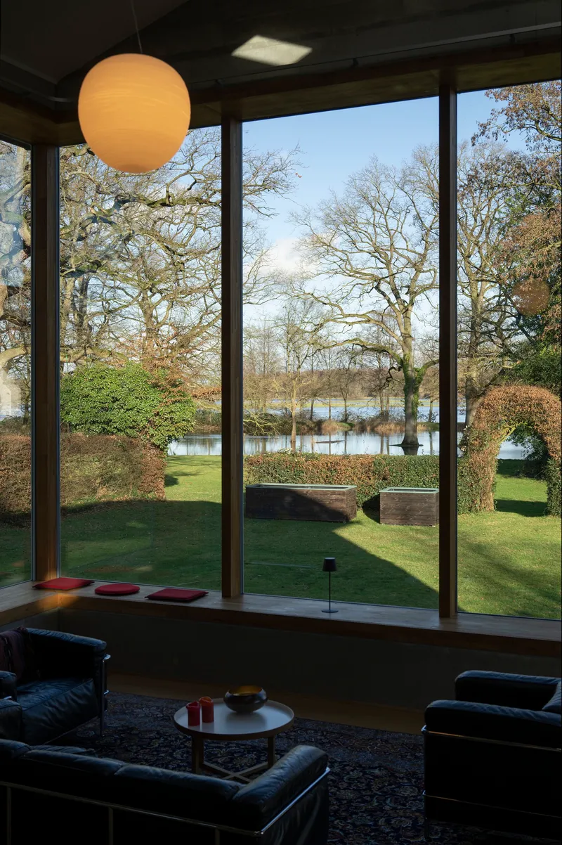 Floor-to-ceiling window framing a view of bare winter trees and a lake beyond a lawn