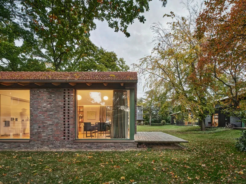 Perforated brick facade and corner glazing beneath a clay tile roof at dusk