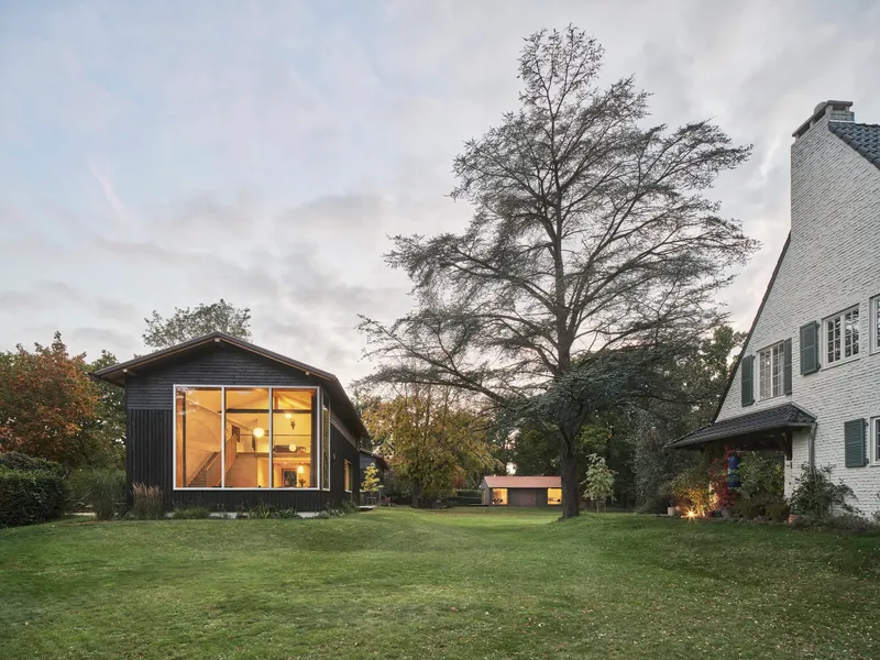 Garden elevation showing two gabled volumes beneath a large deciduous tree at dusk