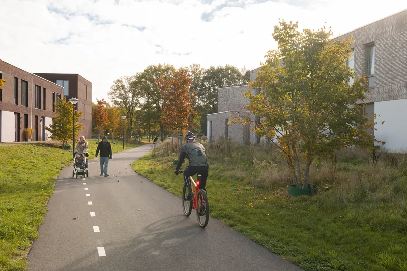 Shared pathway with a cyclist and pedestrians flanked by residential brick facades and autumn trees