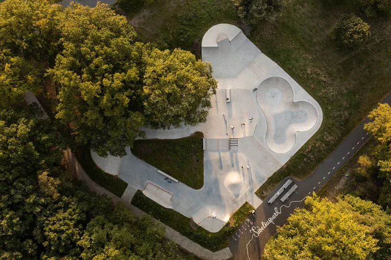 Aerial view of a concrete skate park with curving bowls and ramps surrounded by trees in autumn