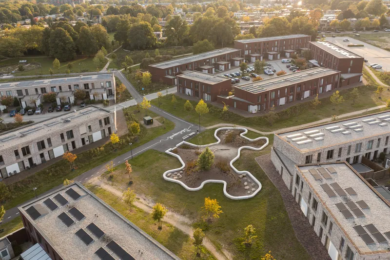 Drone view of a white curvilinear playground set among brick residential buildings and golden fall foliage