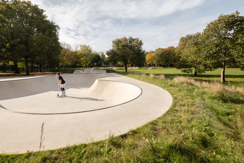 Skateboarder in a curved concrete bowl surrounded by parkland with autumn trees and dry grasses