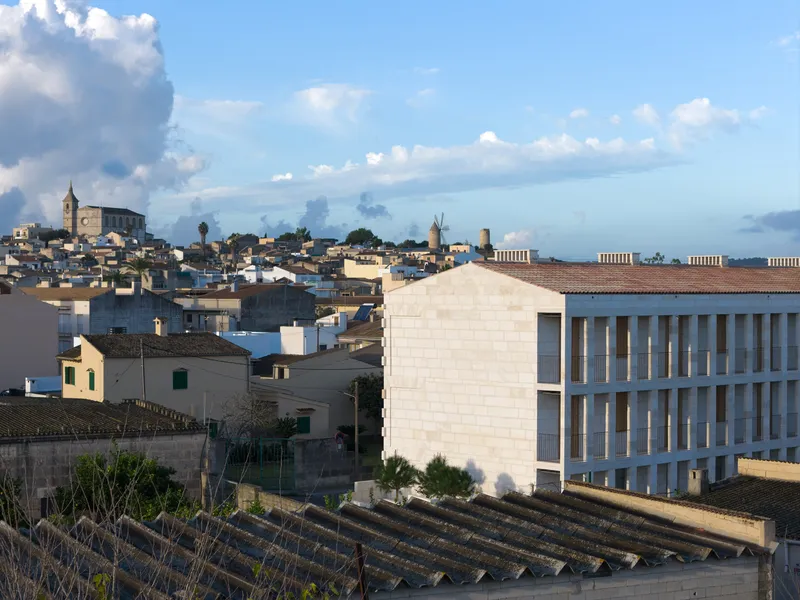 Light stone facade with vertical window openings rising above terracotta rooftops at dusk