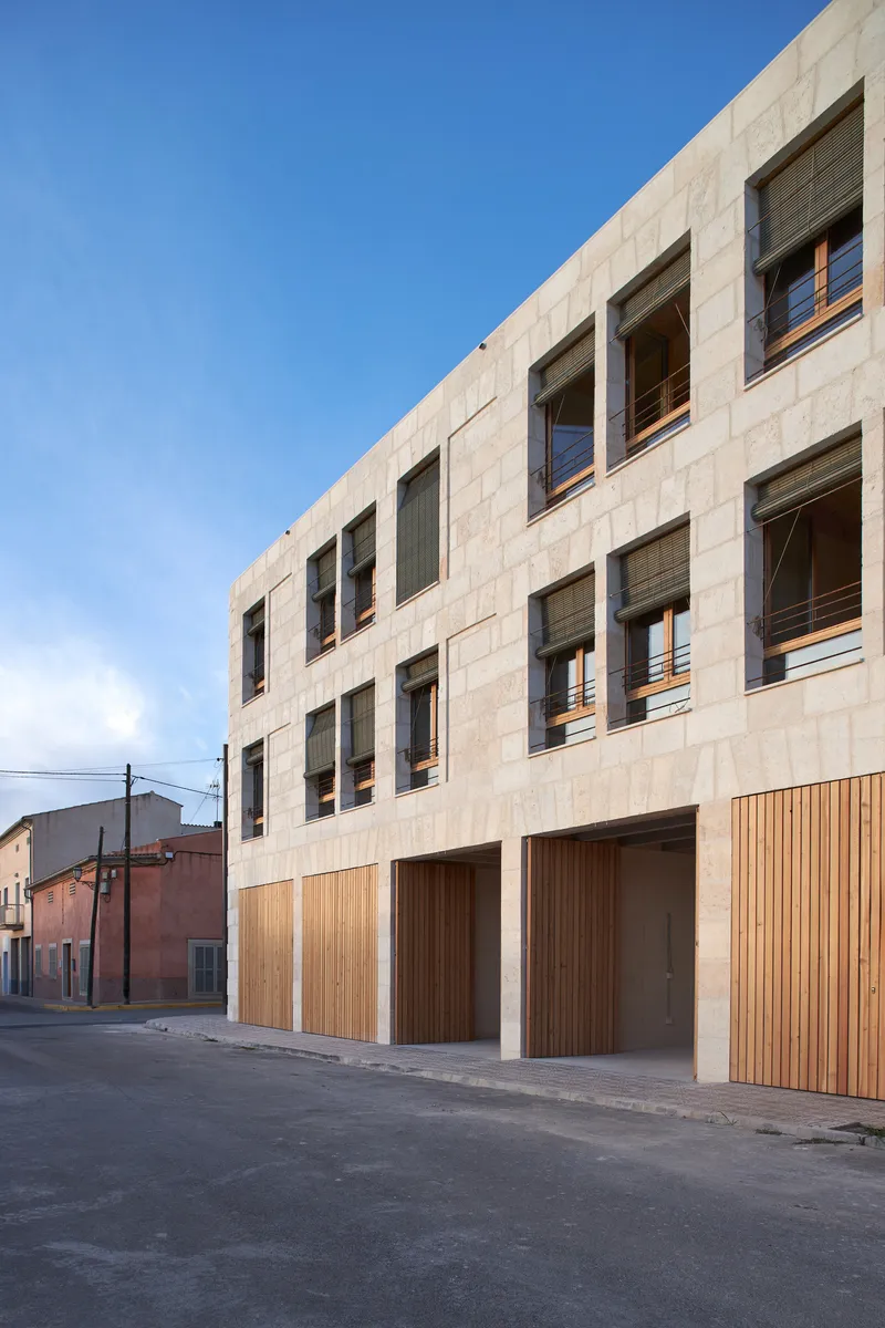 Street-facing facade with vertical timber garage doors beneath punched stone window openings