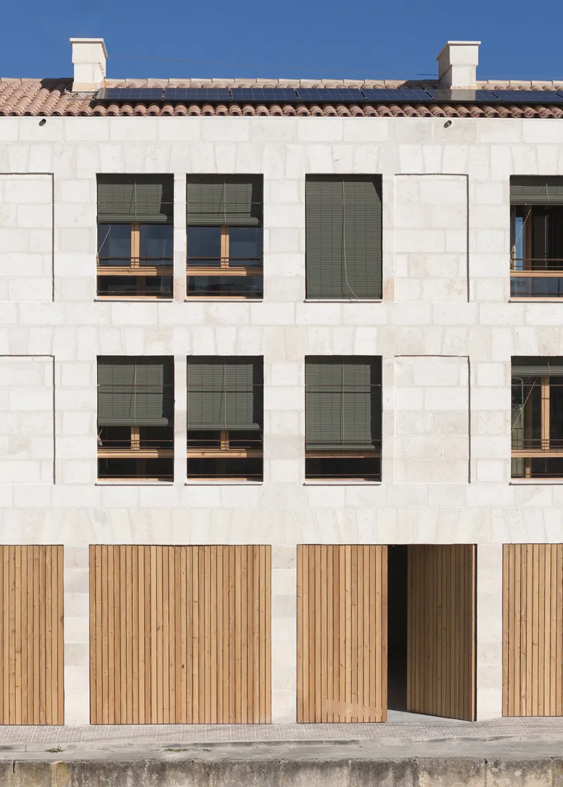 Ground level entry with timber slat doors and punched window openings in pale stone