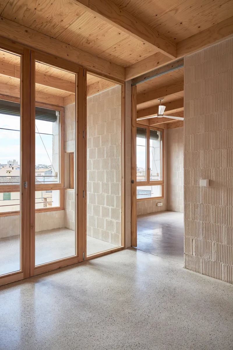 Interior room with exposed timber ceiling beams, terrazzo floor, and white ceramic tile partition alongside timber-framed glazed doors