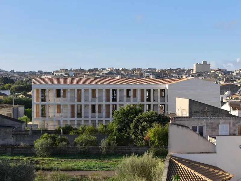 Distant view of the white concrete block facade with red clay tile roof amid surrounding townscape