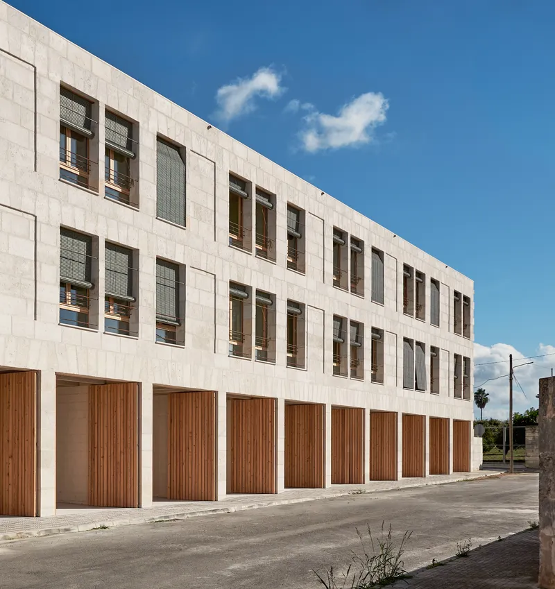 Street-facing facade showing pale stone panels and vertical timber slat shutters at ground level under blue sky