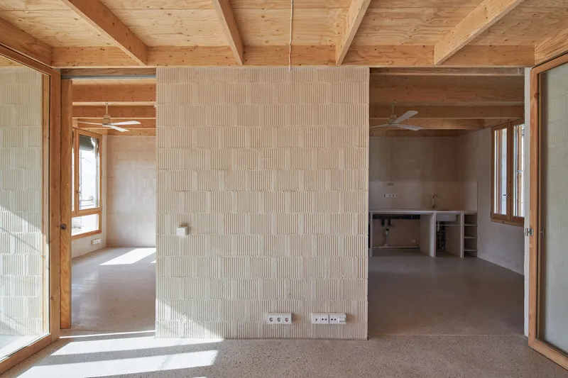 Open interior with exposed timber beams and ribbed hempcrete partition wall dividing the concrete floor space