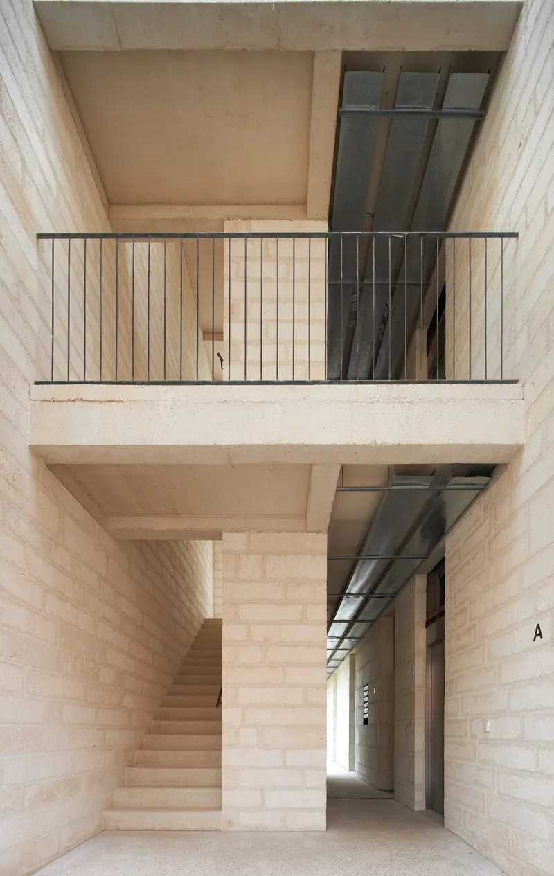 Internal stairwell with pale stone walls, steel balcony railings and glass block windows across two levels