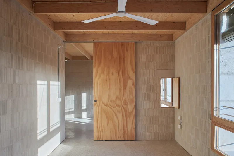 Large plywood sliding door set within a white ceramic tile wall beneath exposed timber beams with afternoon sunlight