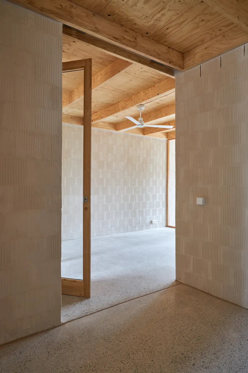 View through a timber-framed doorway into an adjacent room with white ceramic tile walls and ceiling fan above