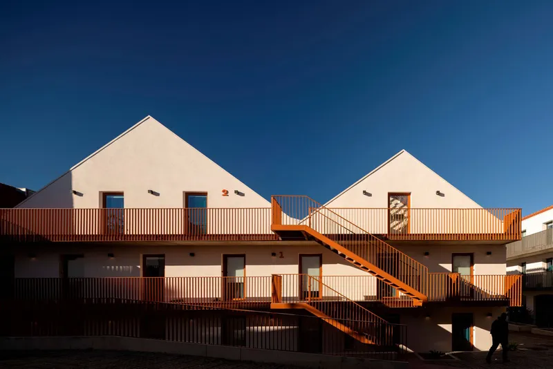 Courtyard facade with white gabled forms and external terracotta metal staircases under blue sky