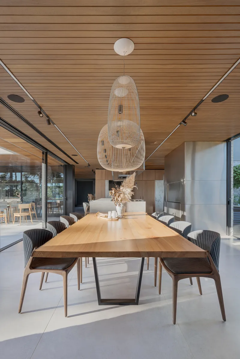 Dining table with pendant light fixture centered beneath continuous slatted wood ceiling and track lighting