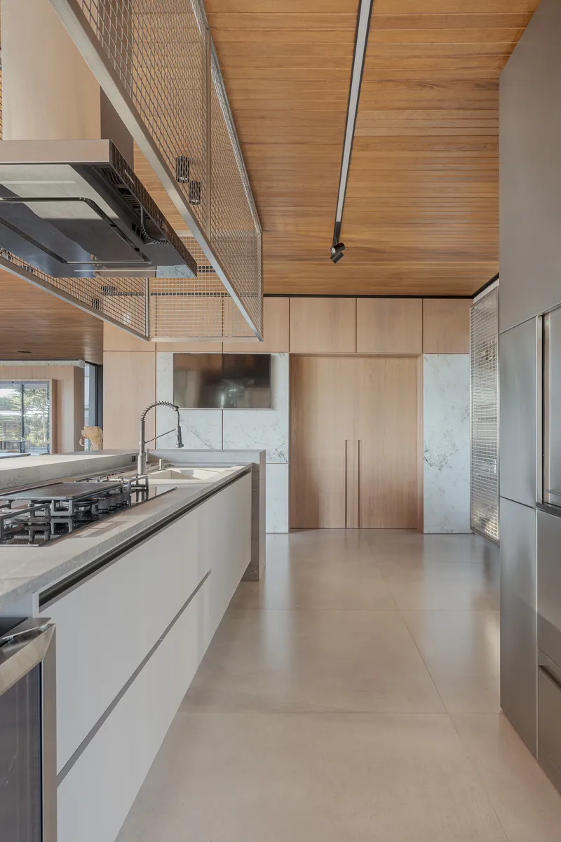 Double-height kitchen with wood-paneled ceiling, metal mesh balustrade, and stone countertops under natural light