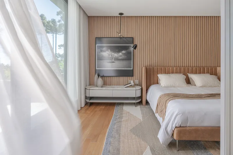 Bedroom with vertical wood slat wall, upholstered headboard, and white curtains filtering daylight