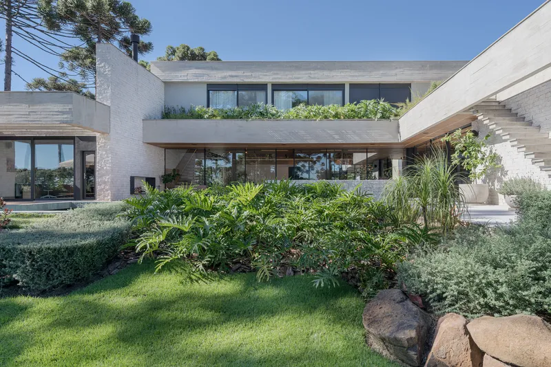Garden view of white brick facade with planted beds and ornamental grasses beneath araucaria pines