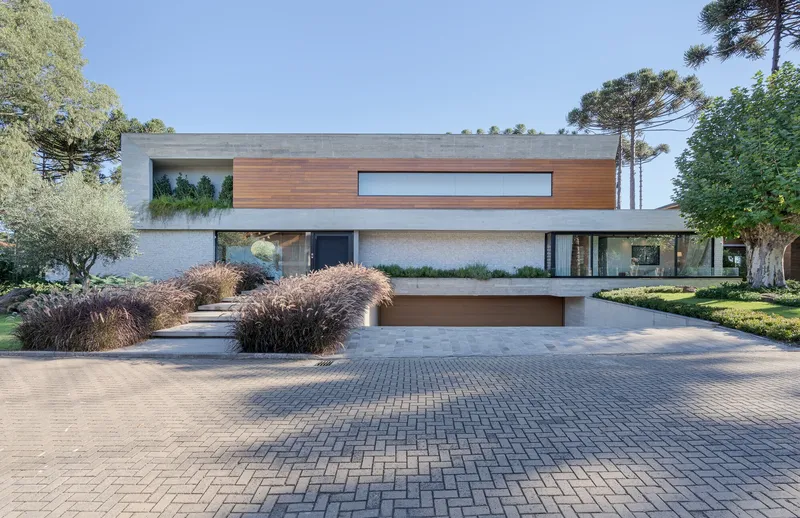 Entry facade with horizontal wood cladding above white brick base and cobblestone driveway with ornamental grasses