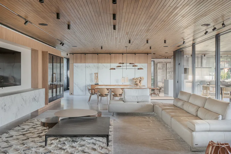Open living and dining area with slatted timber ceiling and pendant lights above light wood flooring