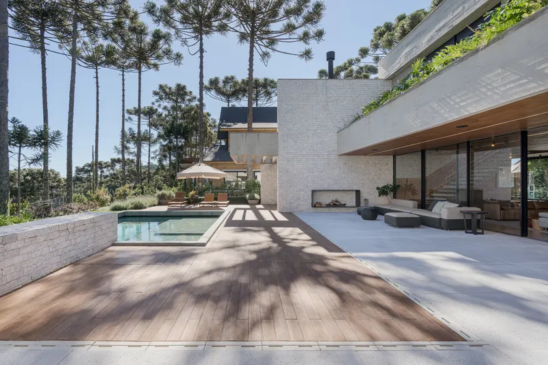 Rear terrace with swimming pool and timber decking casting shadows under midday sun and araucaria pines