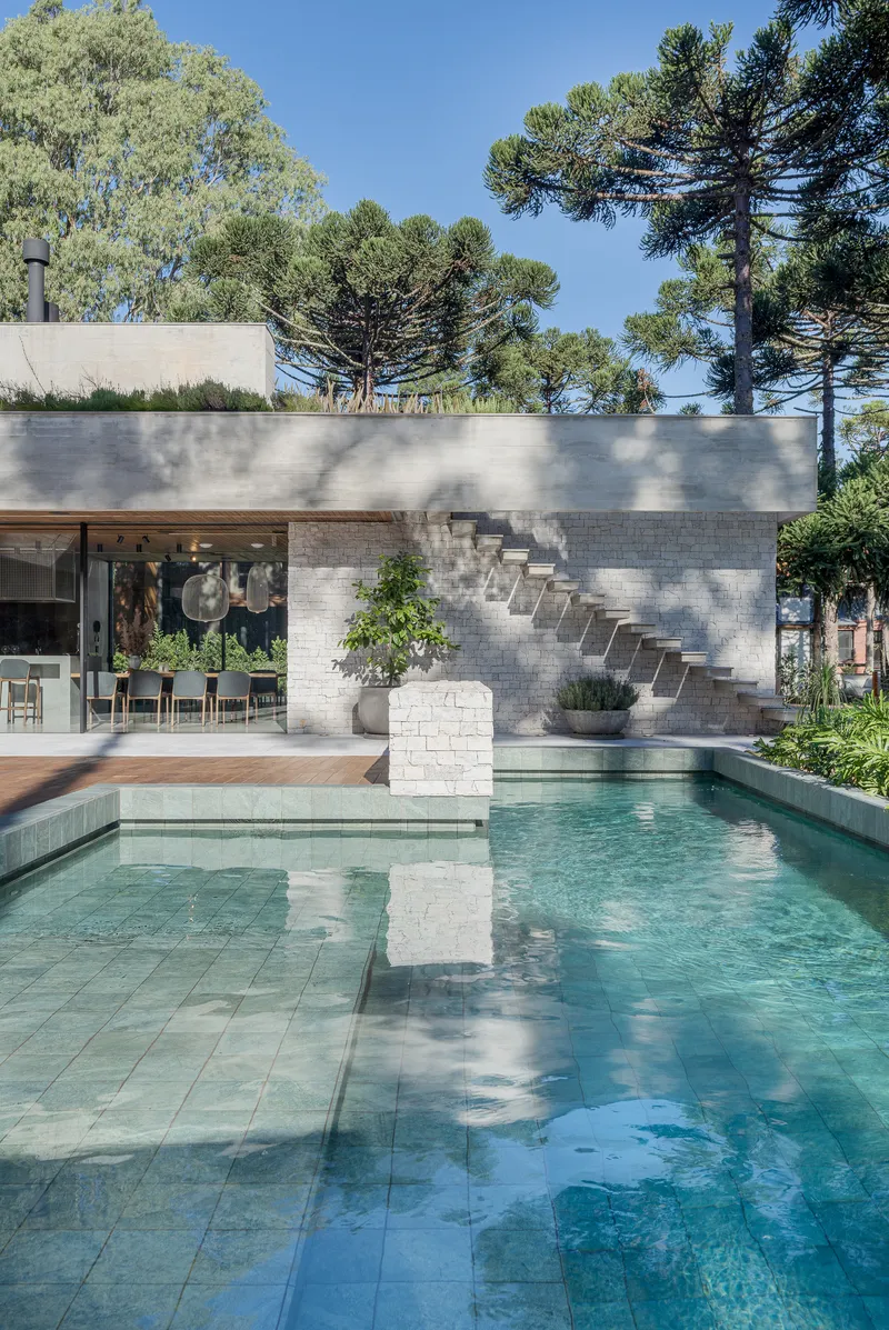 Terrace pool with exterior staircase ascending white masonry wall under dappled tree shade