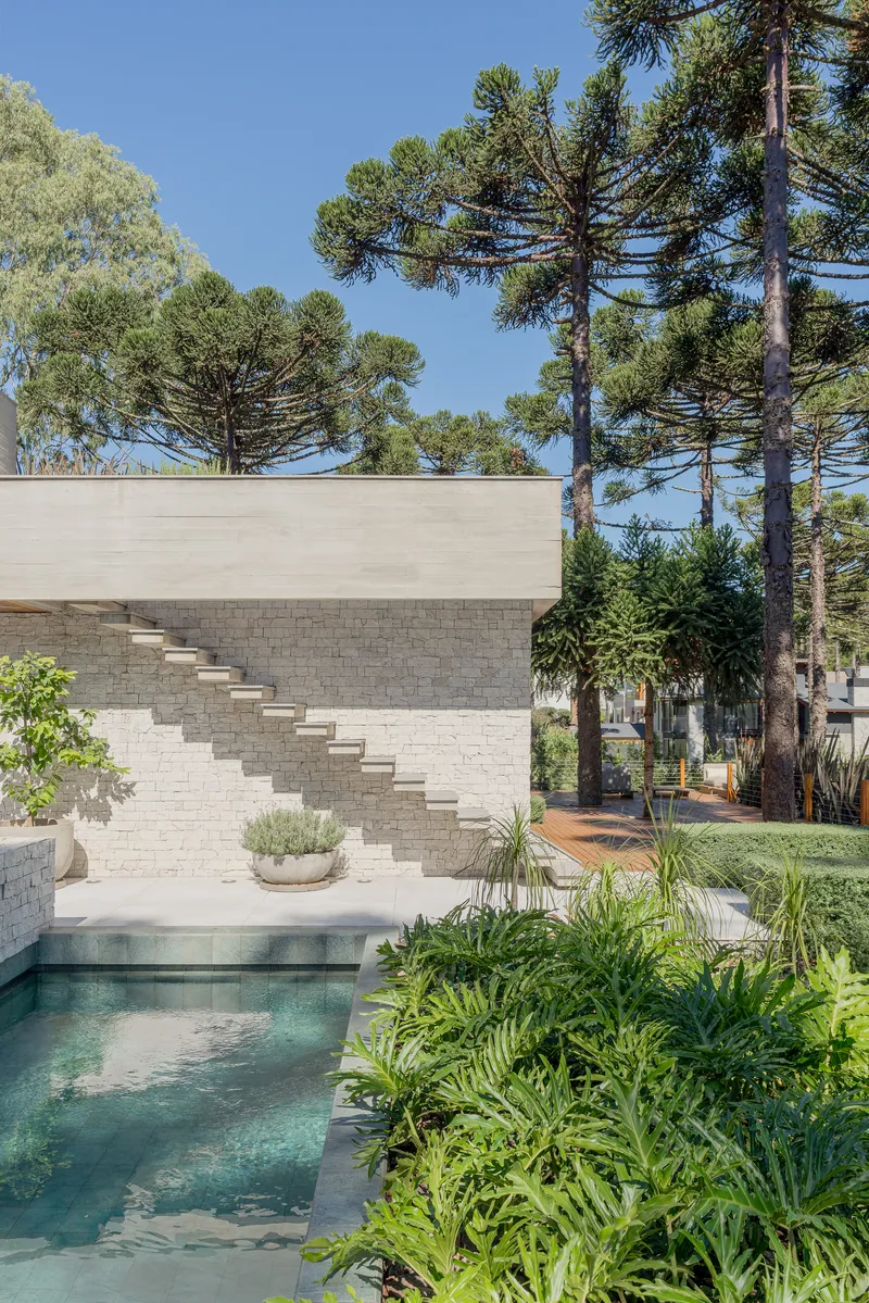 External staircase on white masonry wall beside pool with tropical planting and pine canopy