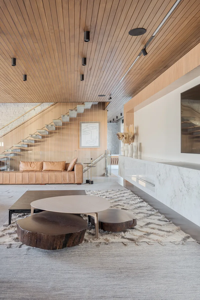 Double-height living room with slatted timber ceiling and floating glass staircase under pendant lights
