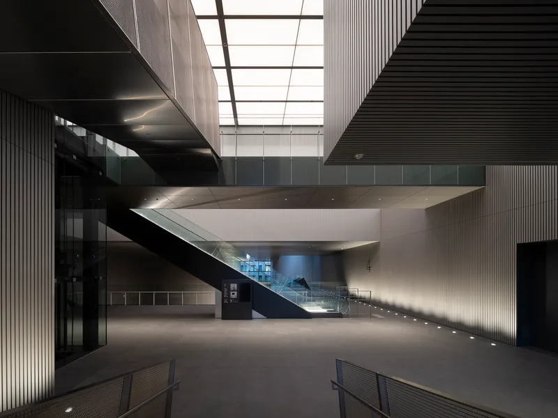 Ground floor lobby with cantilevered stair platform hovering above under a gridded skylight